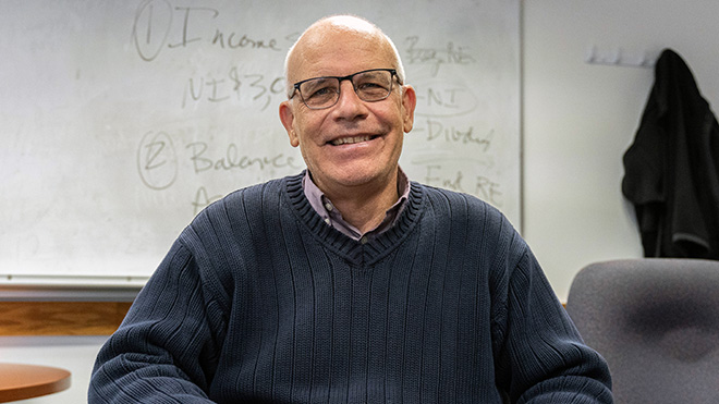 John McQuilkin sitting in his office in front of a whiteboard
