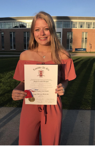Person standing in front of building holding diploma.