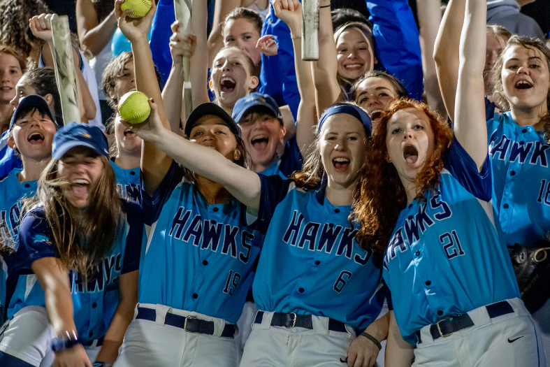 Softball players in Hawks uniforms, cheering.