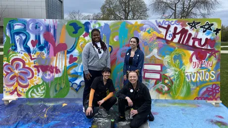 Four people pose in front of the Unity Mural