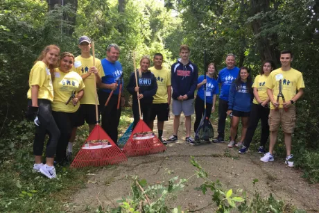 Group photo of students and president holding rakes on a path.