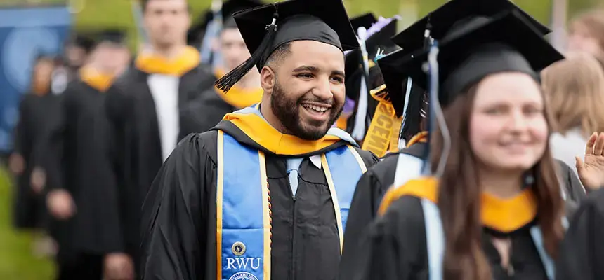 Graduate student in commencement regalia walking in the 2025 ceremony.