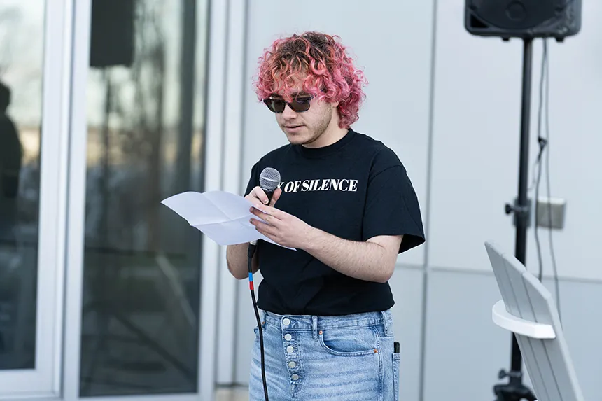 A student wearing a Day of Silence T-shirt speaks into a microphone. 