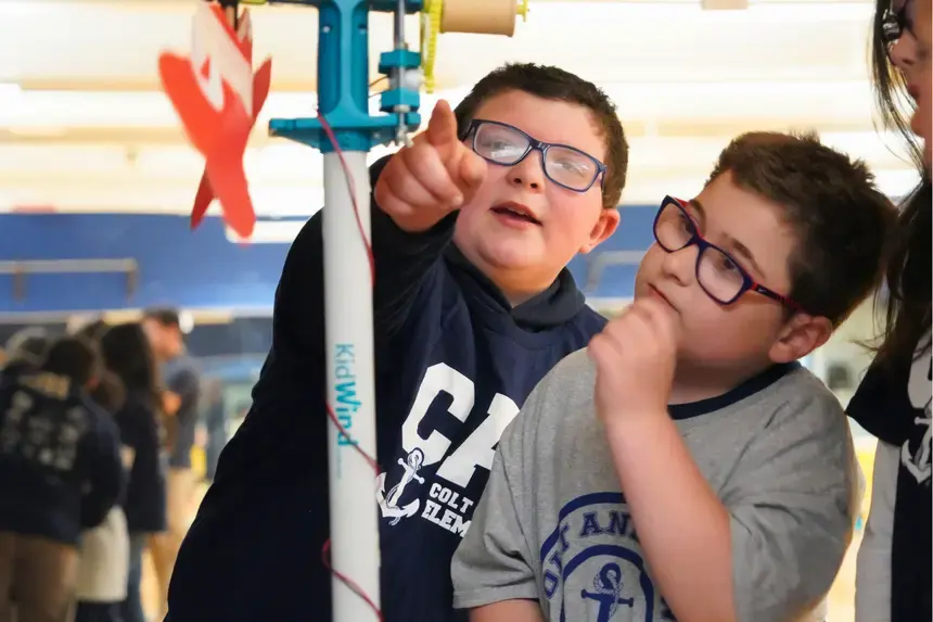 Two fourth graders examine a wind turbine alongside professionals.