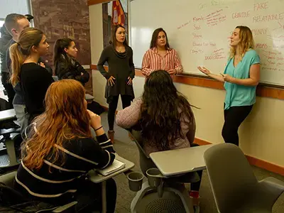 A group of students standing in a circle talking in front of a whiteboard