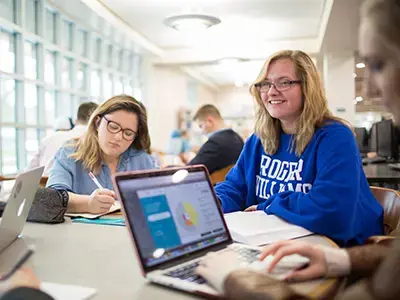 A group of students working at a table on computers and smiling